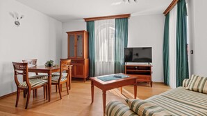 Ein eingerichtetes Wohnzimmer mit Holzesstisch, Stühlen, einer Couch, einem Fernseher und einem Schrank.