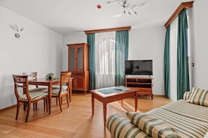 Ein eingerichtetes Wohnzimmer mit Holzesstisch, Stühlen, einer Couch, einem Fernseher und einem Schrank.