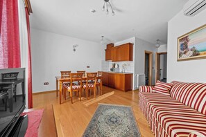 Ein Wohnzimmer mit Sofa, einem Esstisch mit Stühlen, einer Küchenzeile und einem Bild an der Wand.