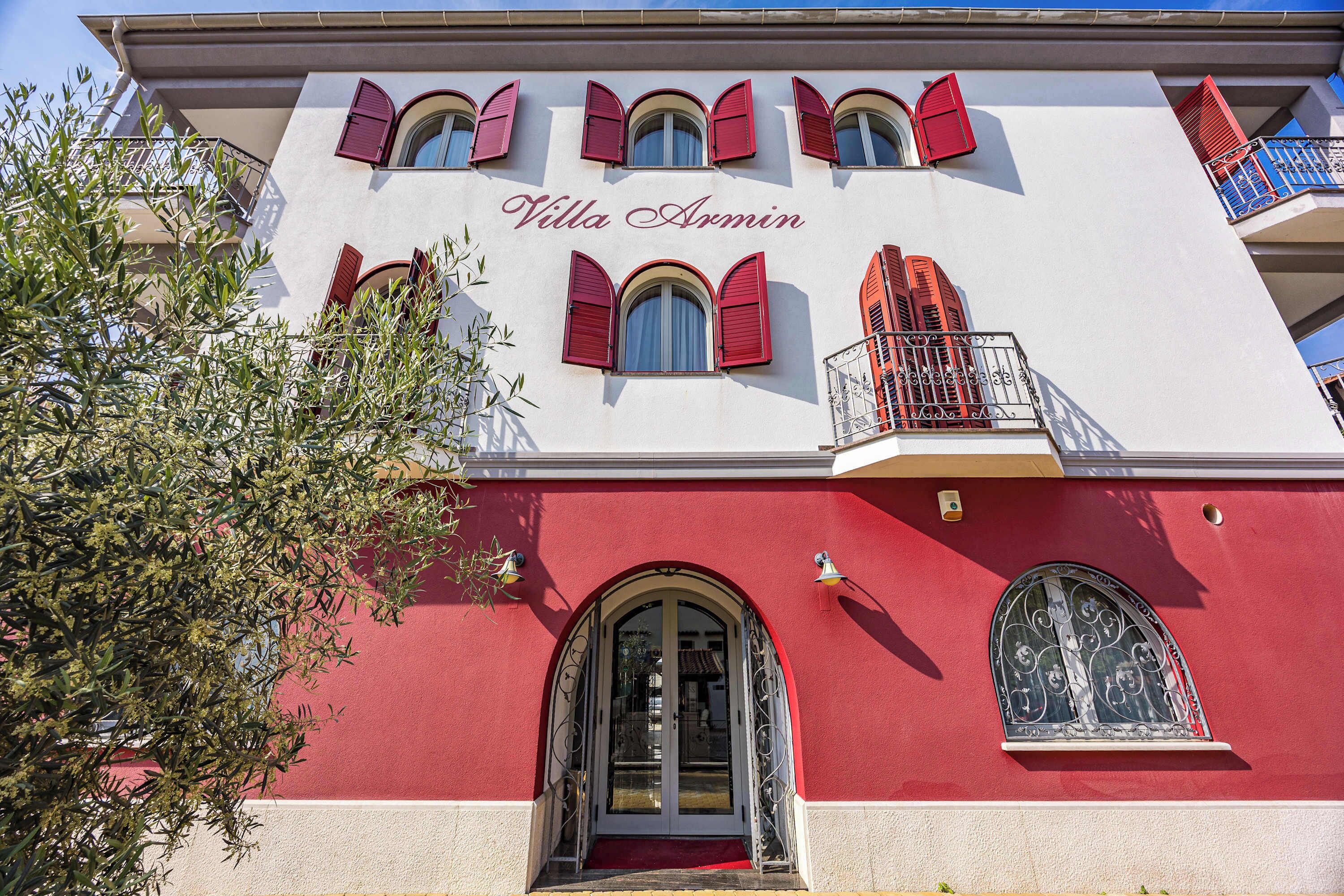 A building with a red and white facade, arched windows, and balconies with red shutters.