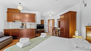 A hotel room with a bed, a sofa, a kitchen area with wooden cabinets, a television, and a dining table. - Studio apartment for 2 in Villa Armin (Rovinj)