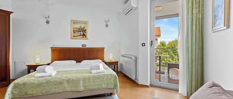 Quarto com cama, mesa de cabeceira, radiador, janela com vista e varanda.