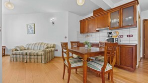 A kitchen with wooden cabinets, a dining table with chairs, a sofa, and a framed picture on the wall. - Studio apartment for 2 in Villa Armin (Rovinj)