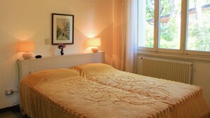 Quarto com uma cama, duas luminárias de cabeceira, um quadro na parede e uma janela com cortinas.