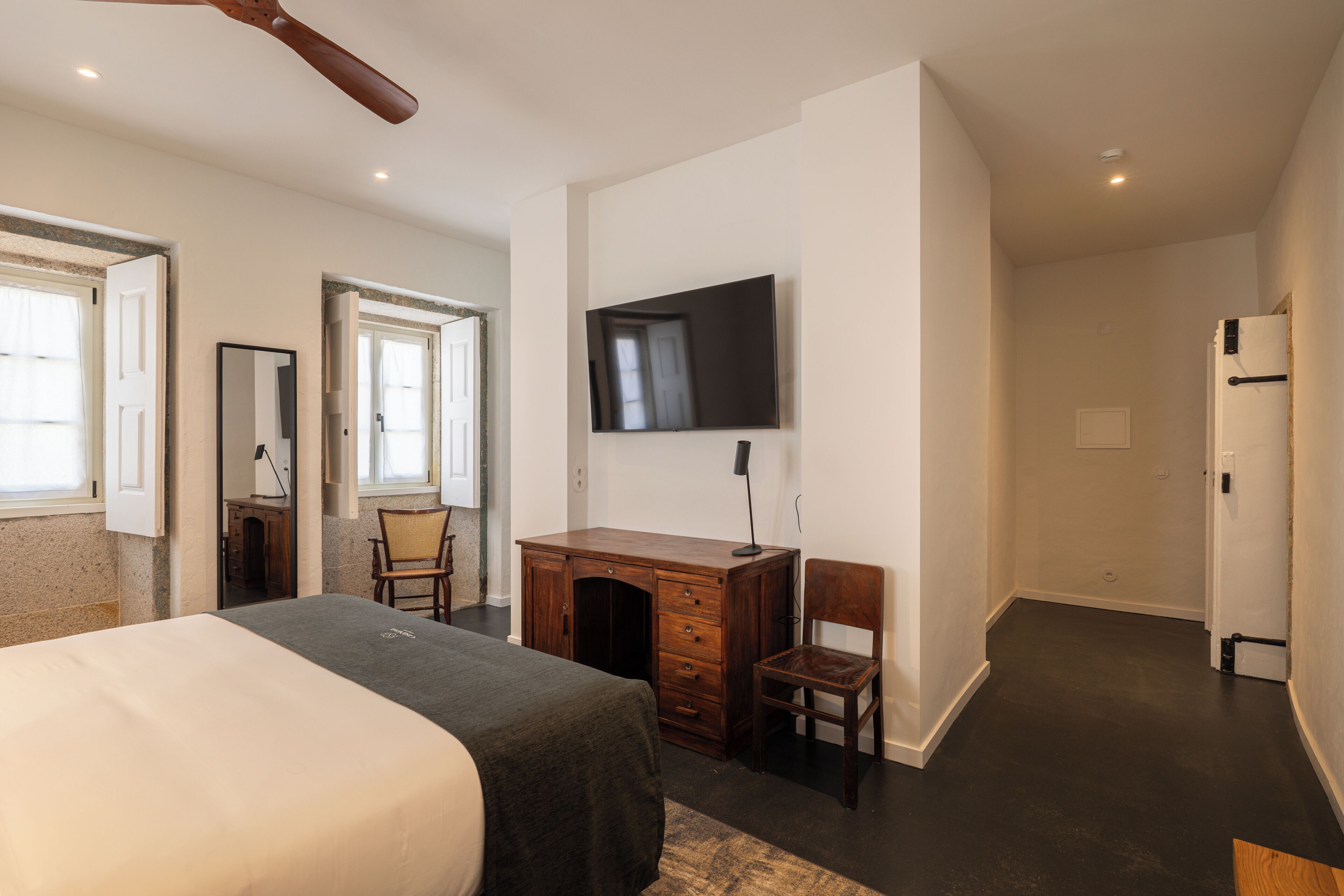 A bedroom with a bed, a desk, a chair, a TV, and a door.