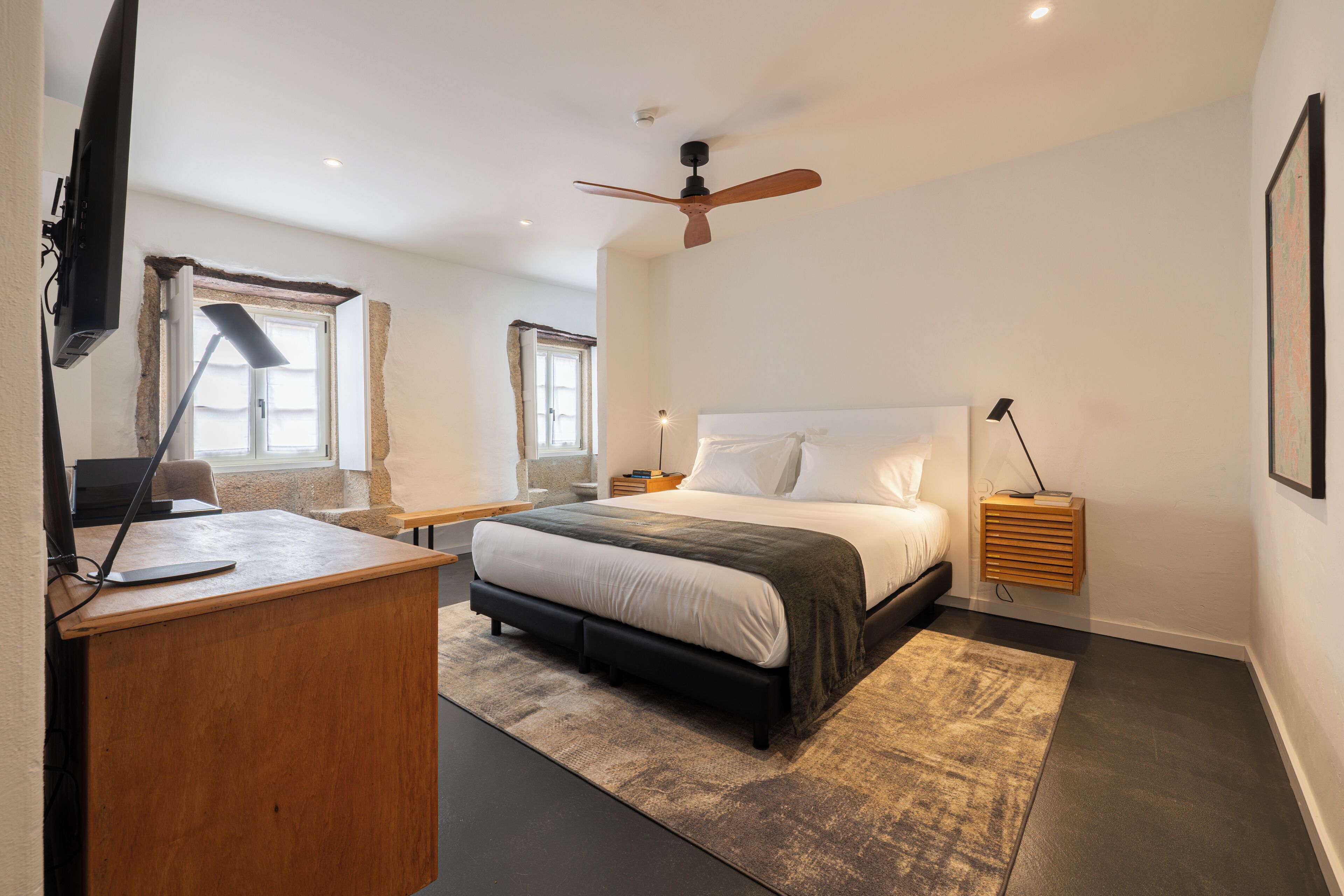 Une chambre à coucher comprenant un lit, un bureau, une chaise, un ventilateur de plafond et une fenêtre.