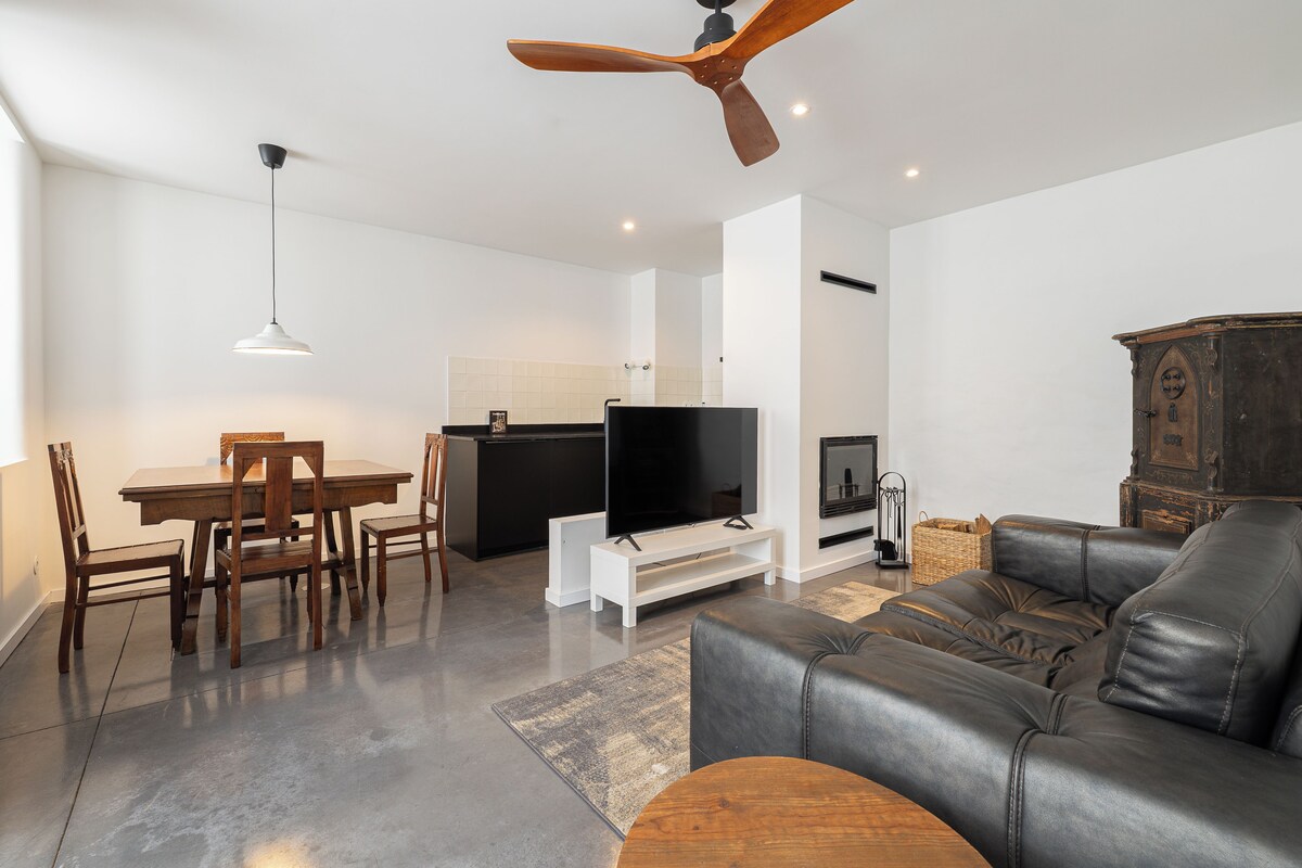 A modern living room with a dining area, a leather sofa, a TV, and a ceiling fan.