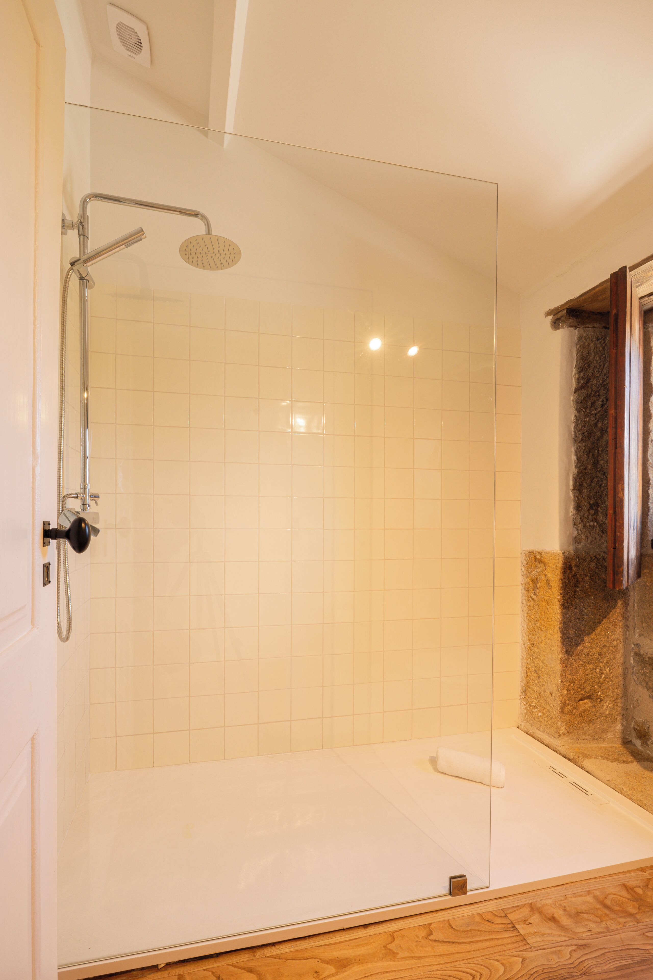 Een douche met glazen wand, een handdouche en een bedieningspaneel aan de muur.