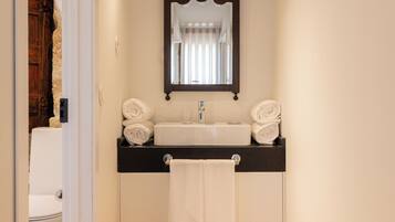 A bathroom with a wooden floor, a white sink, a black countertop, and a mirror above the sink.