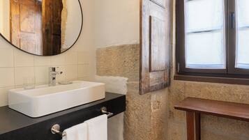 Un baño con un lavabo blanco, un espejo redondo, una puerta de madera y una ventana con cortinas.