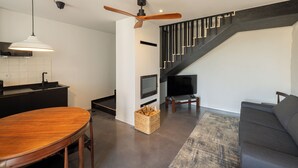 Una sala de estar moderna con una escalera oscura, una mesa de comedor de madera y un televisor de pantalla plana.