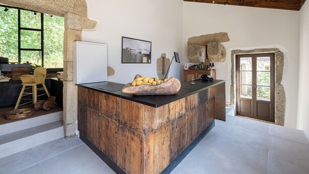 Una cocina rústica con una isla de madera, paredes de piedra y un ventanal con vistas al verdor.