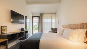 Una habitación de hotel moderna con una cama grande, un televisor de pantalla plana montado en la pared, un escritorio con una silla y vistas al exterior a través de la ventana.