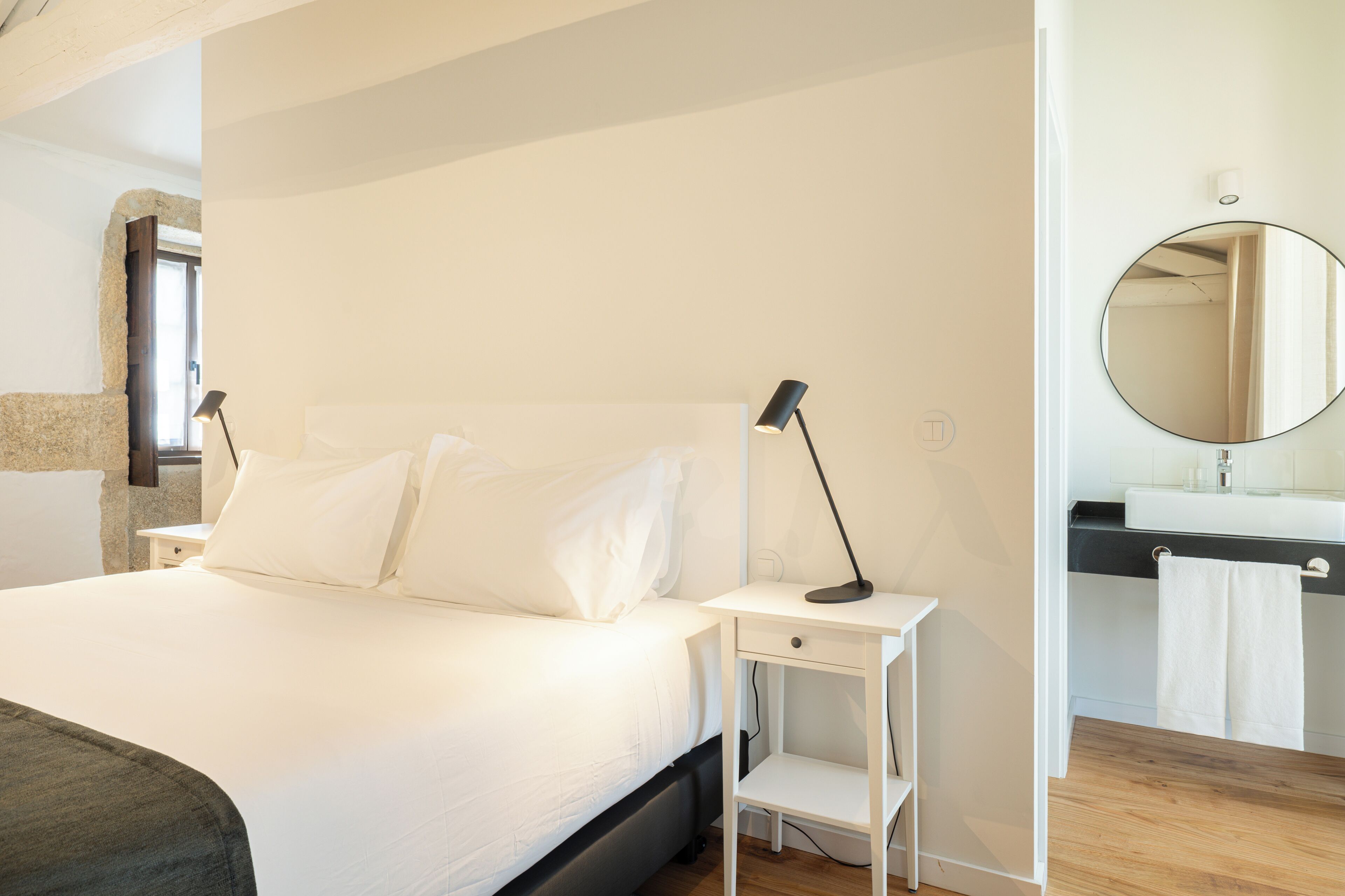 Une chambre à coucher comprenant un lit, des tables de chevet, un miroir et une salle de bain avec un lavabo et un porte-serviettes.
