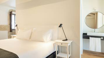 Une chambre à coucher comprenant un lit, des tables de chevet, un miroir et une salle de bain avec un lavabo et un porte-serviettes.