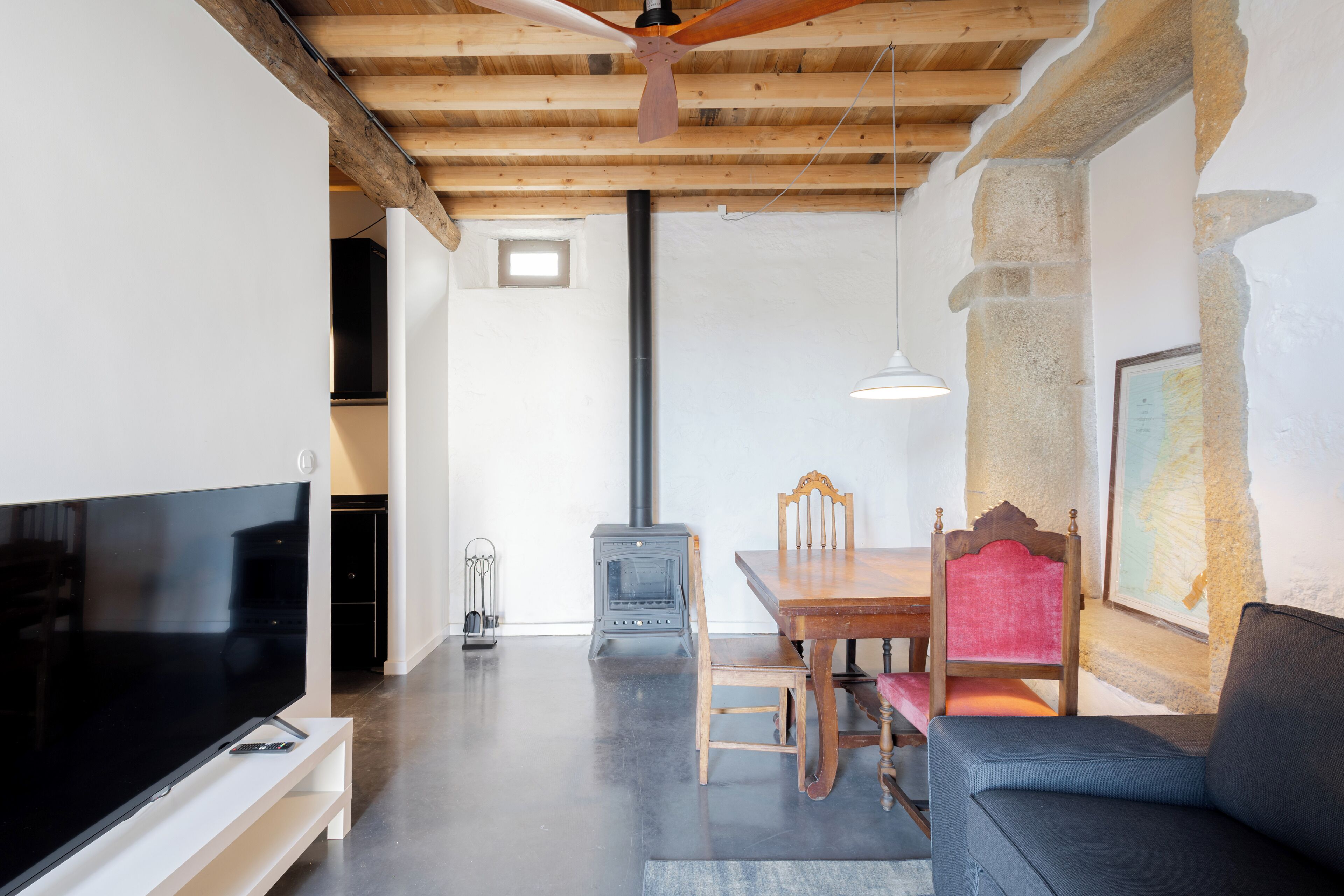 A modern living room with a flat-screen TV, wooden furniture, a stone wall, and a ceiling fan.
