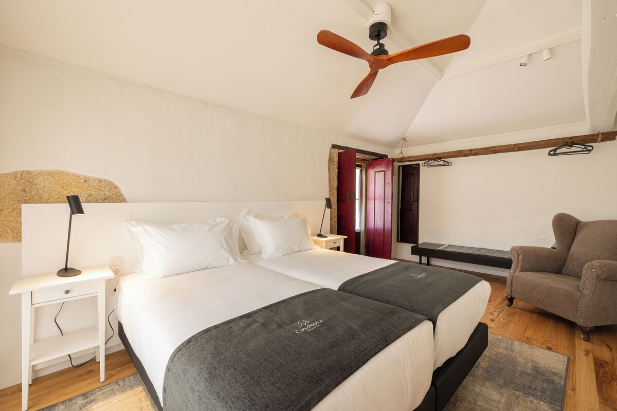 A bedroom with two beds, a ceiling fan, a nightstand, a chair, and a wooden bench.