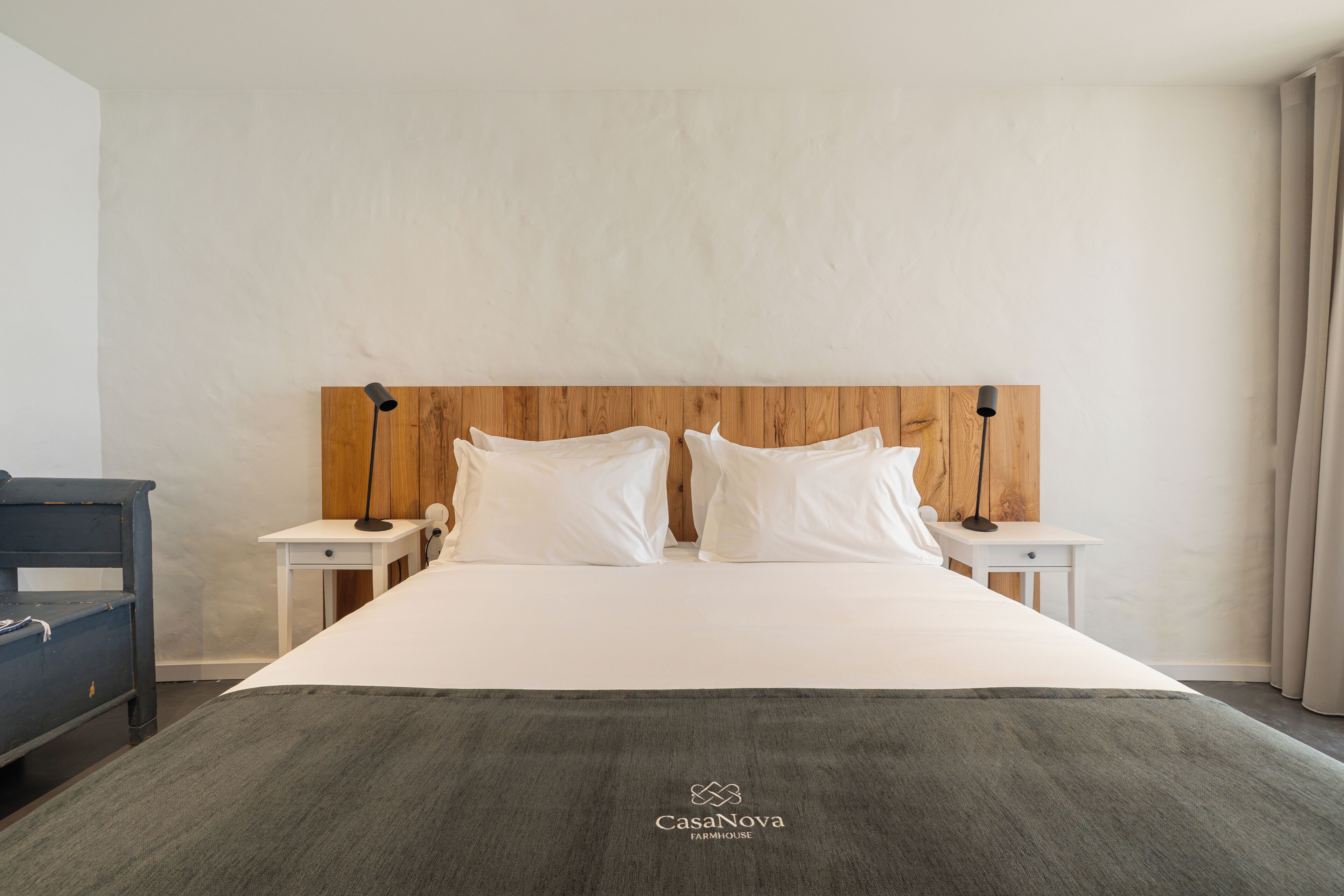 A hotel room with a wooden headboard, white bedding, two bedside tables with lamps, and a grey throw blanket.