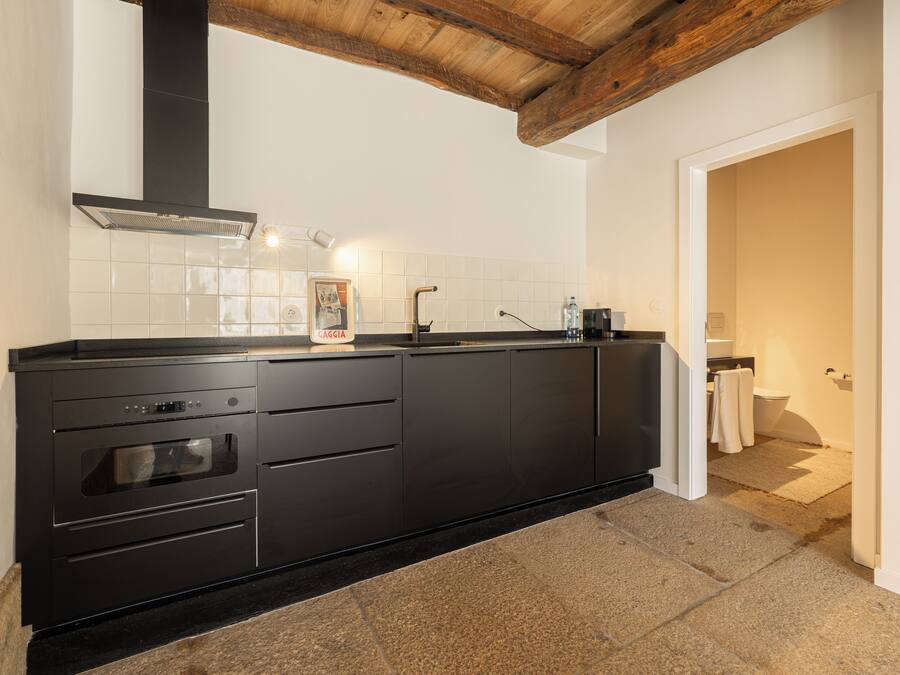 A modern kitchen with black cabinetry, a built-in oven, and a stainless steel range hood.