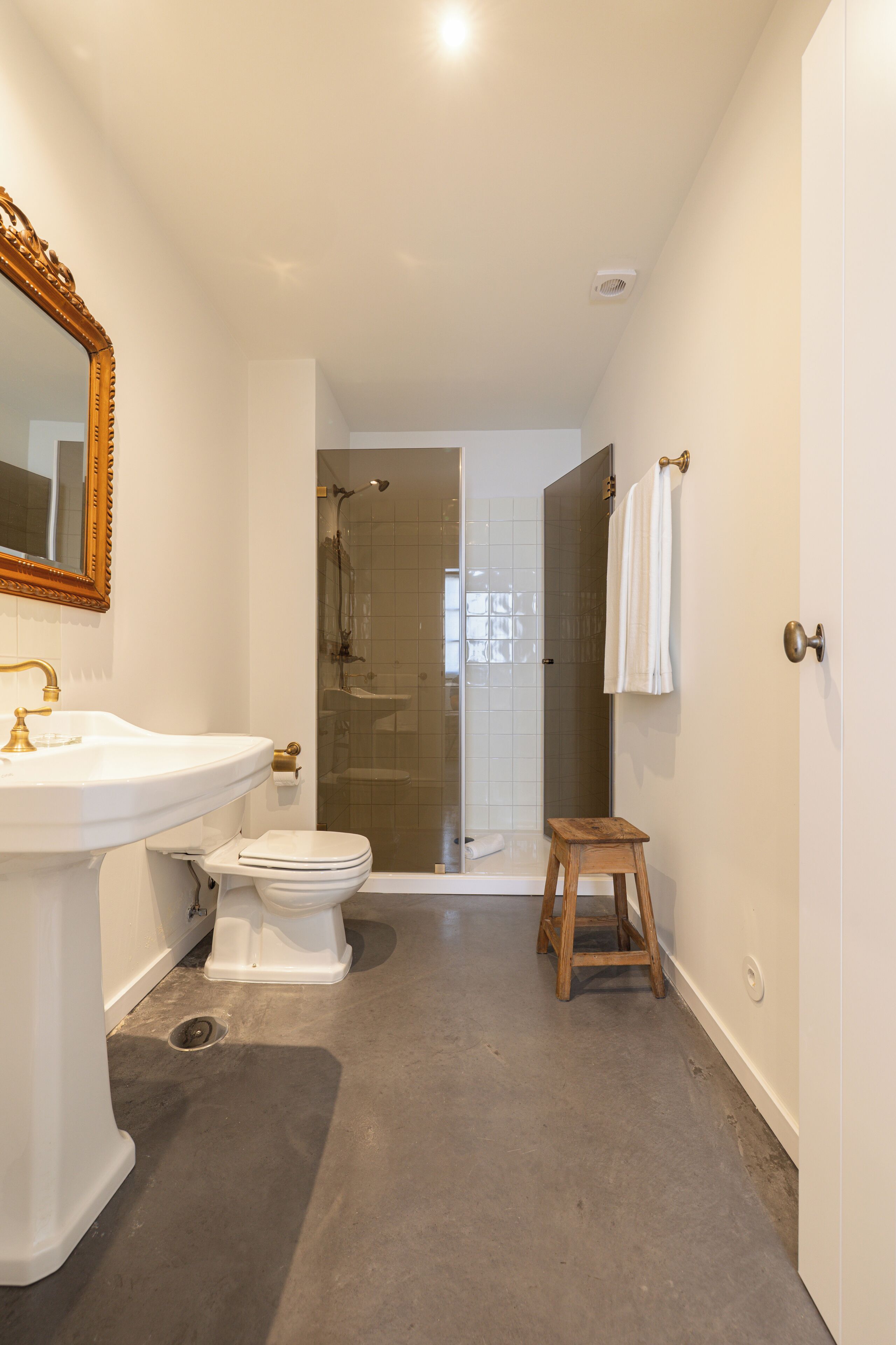 A bathroom with a sink, toilet, shower, and a wooden stool.