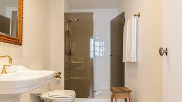 A bathroom with a sink, toilet, shower, and a wooden stool.