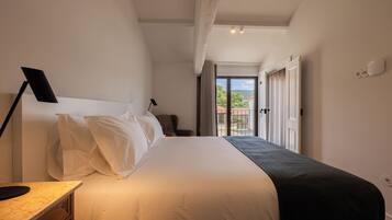 A hotel room with a large bed, a desk with a lamp, a chair, and a view of the outdoors through a door.