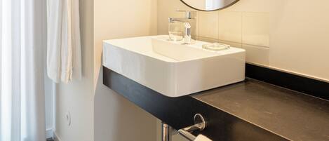 A modern bathroom with a white sink, a large mirror, and a towel rack.