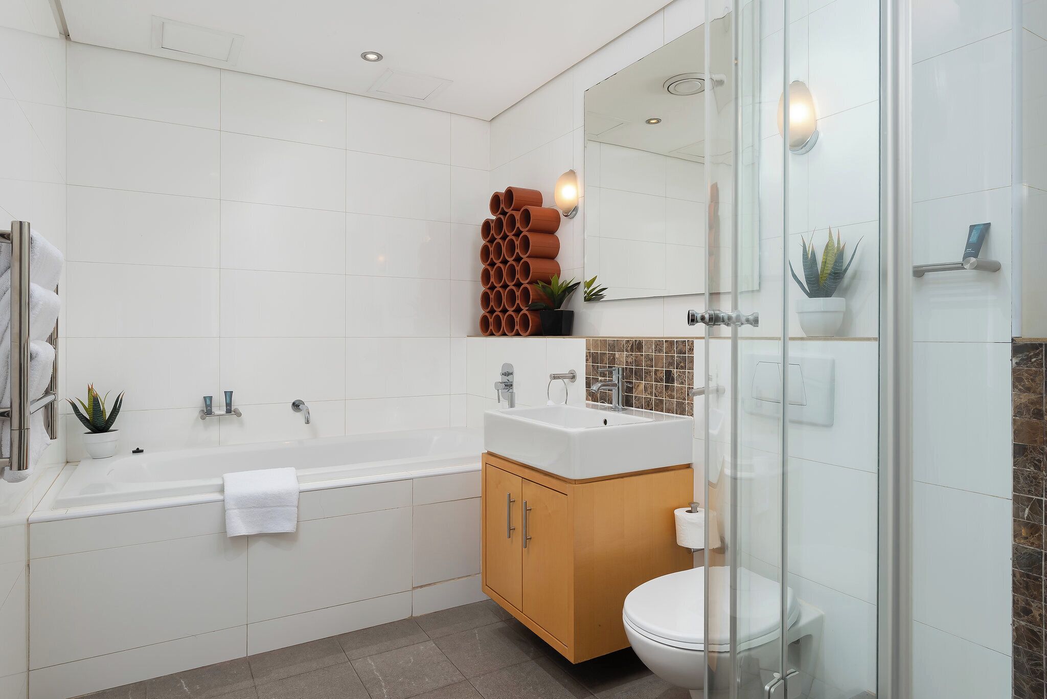Un bagno moderno con vasca, lavandino e toilette. Sono presenti piante e uno specchio.