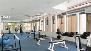 A gym with exercise equipment, a blue carpet, and large windows. - Cartwrights Corner Executive Apartment (Cape Town)