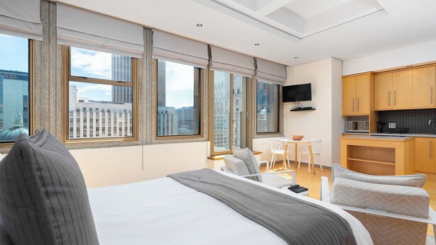 A modern hotel room with a large bed, a desk, a chair, and a kitchenette. - Cartwrights Corner Executive Apartment (Cape Town)