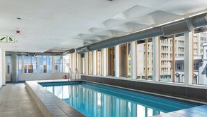 An indoor swimming pool with clear glass walls, a tiled floor, and a view of the cityscape. - Cartwrights Corner Executive Apartment (Cape Town)