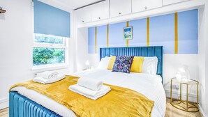 A modern hotel room with a large bed, a window with curtains, a bedside table with a lamp, and a wall with a decorative panel. - Wimbledon/Discount/Close to AELTC&Station/En-Suite (London)