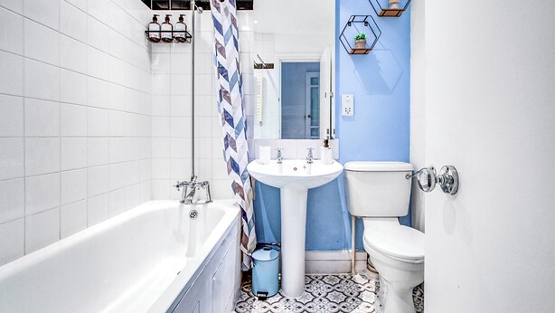 Un baño moderno con una bañera y un lavamanos blancos, además de un inodoro. Hay estantes hexagonales decorativos en la pared.