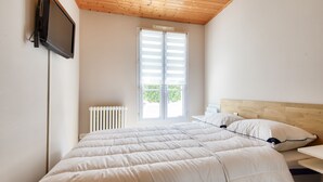 Et soveværelse med en seng, et fjernsyn ophængt på væggen, et vindue med persienner og en radiator.