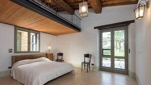 Ein Schlafzimmer mit einem großen Bett, zwei Stühlen, einer Holzbalkendecke und einer Balkontür.
