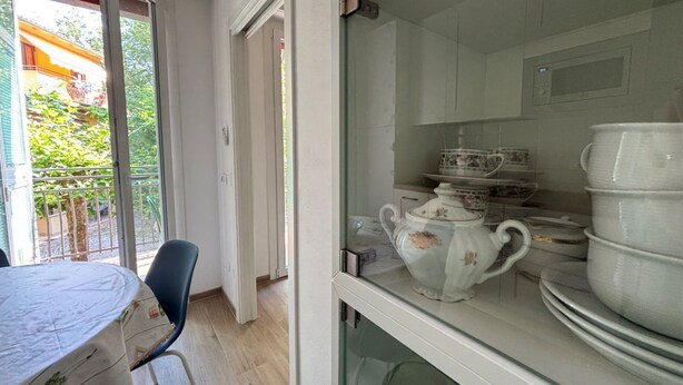 Una stanza con un tavolo da pranzo, sedie, una vetrina con piatti in ceramica bianca e vista sul verde all'esterno.