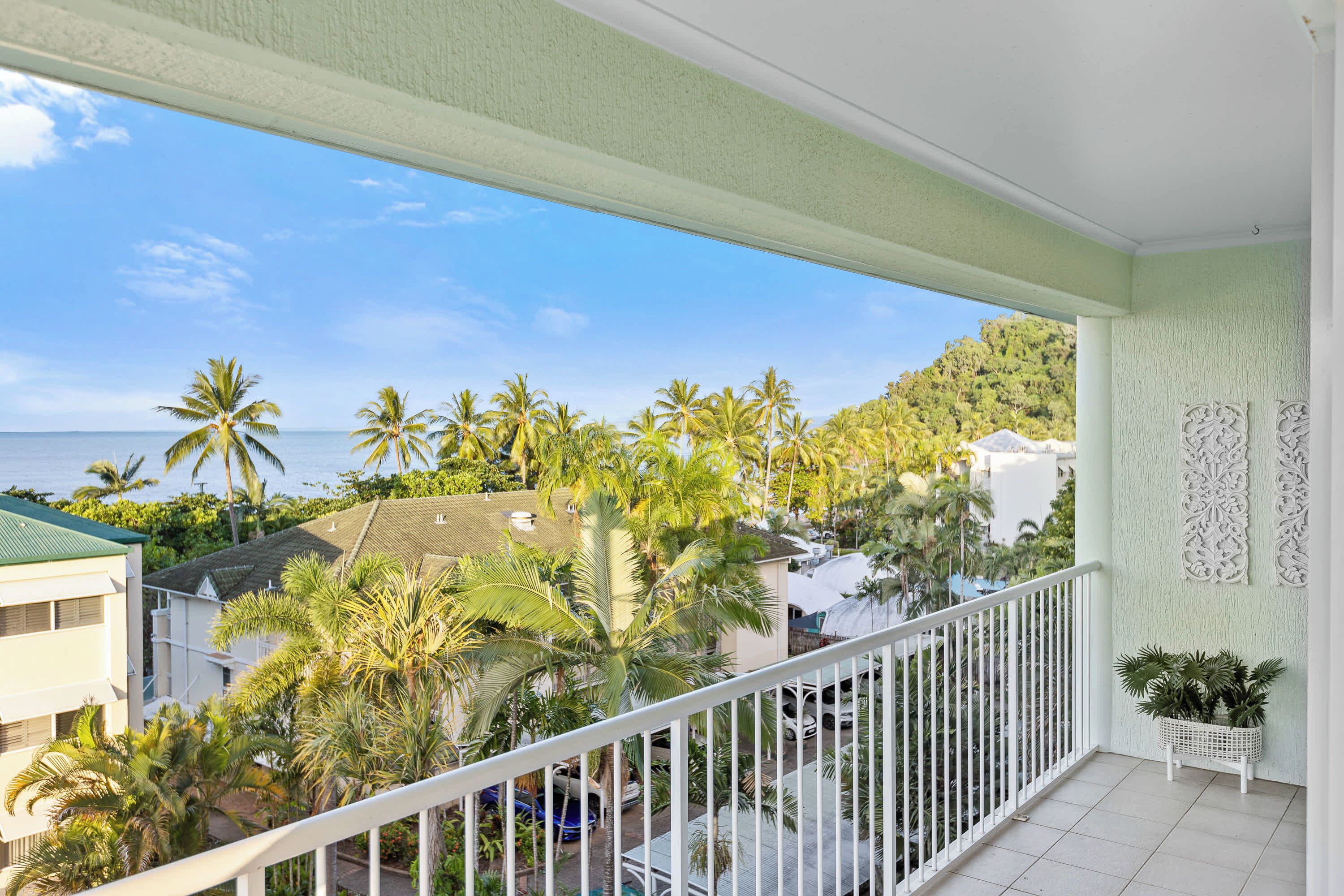 A balcony with a view of a beach, palm trees, and a white railing.
