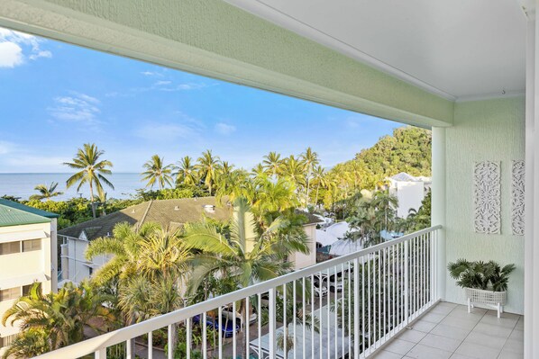 A balcony with a view of a beach, palm trees, and a white railing.