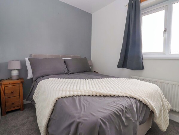 A bedroom with a bed, a bedside table with a lamp, a window with curtains, and a radiator.