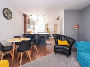 A modern living room with a dining area, a kitchen in the background, and a blue sofa.