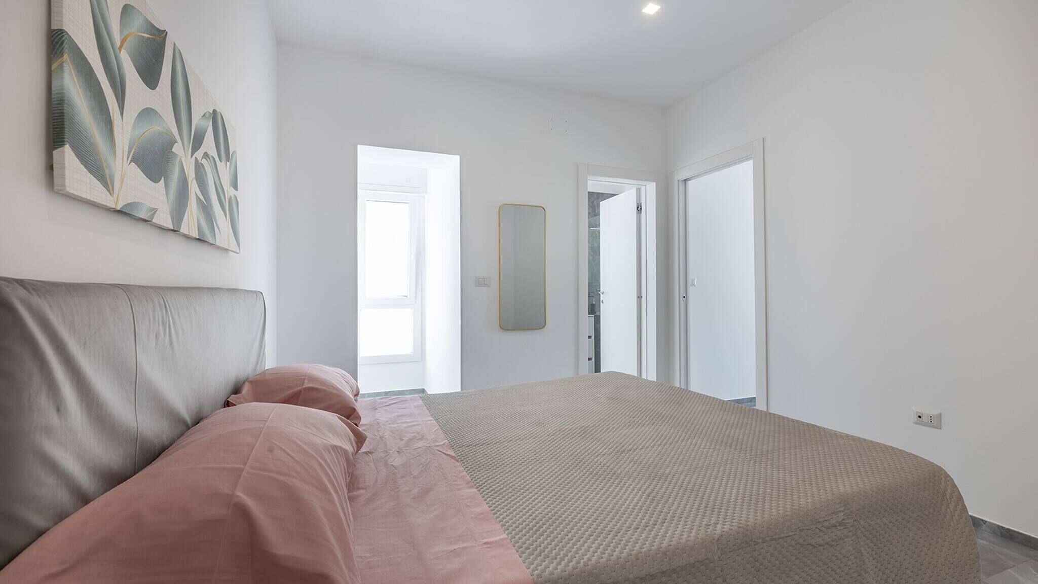 A bedroom with a bed, a large mirror, and a door leading to another room.