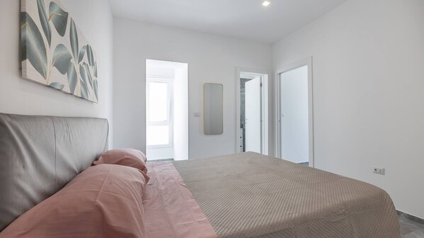 A bedroom with a bed, a large mirror, and a door leading to another room.