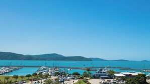 Un puerto deportivo con barcos amarrados, un cielo azul despejado y un paisaje montañoso al fondo.