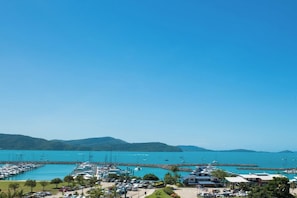 A marina with boats docked, a clear blue sky, and a hilly landscape in the background. - Airlie On Airlie 1 Bedroom (Airlie Beach)