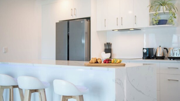 Una cocina moderna con armarios blancos, un refrigerador de acero inoxidable, una encimera de mármol y taburetes de bar.