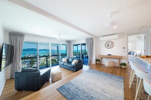 A spacious living area with a balcony, a sofa, a coffee table, and a dining area with bar stools. - Airlie On Airlie 1 Bedroom (Airlie Beach)