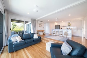 A modern living room with a sofa, a coffee table, and a kitchen area in the background. - Airlie On Airlie 1 Bedroom (Airlie Beach)