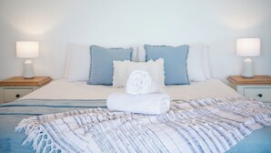 Una cama bien hecha con una toalla enrollada, dos almohadas y una colcha a rayas.