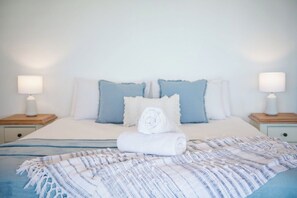 A neatly made bed with a rolled towel, two pillows, and a striped blanket. - Airlie On Airlie 1 Bedroom (Airlie Beach)