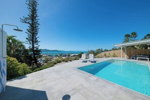 A swimming pool with a view of the sea and mountains, surrounded by a patio area with lounge chairs. - Airlie On Airlie 1 Bedroom (Airlie Beach)